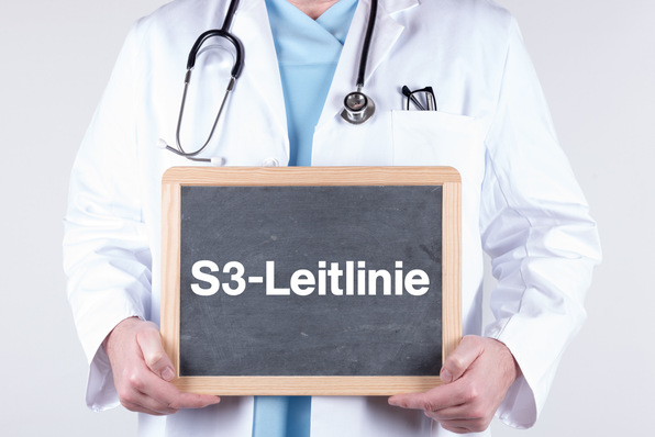 „Mediziner in weißem Kittel und Stethoskop präsentiert ein Schild mit der Aufschrift ‚S3-Leitlinie‘, symbolisiert die Anwendung evidenzbasierter Richtlinien in der medizinischen und juristischen Begutachtung. - © HNFOTO - stock.adobe.com